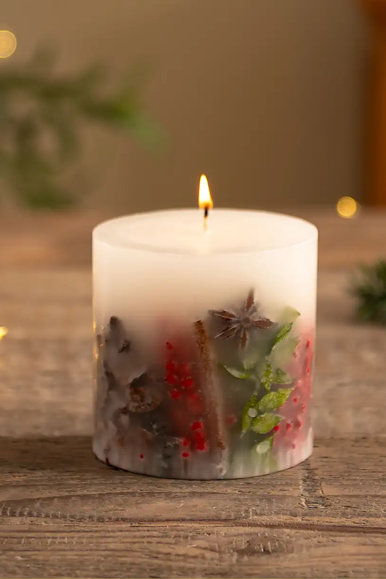A white inclusion candle with star anise, cinnamon, pine, and leaves