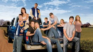 The cast of Friday Night Lights standing in and around a pickup truck on a road