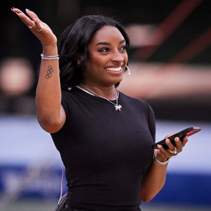 a black woman with short, dark hair wearing a black t-shirt and raising her right hand