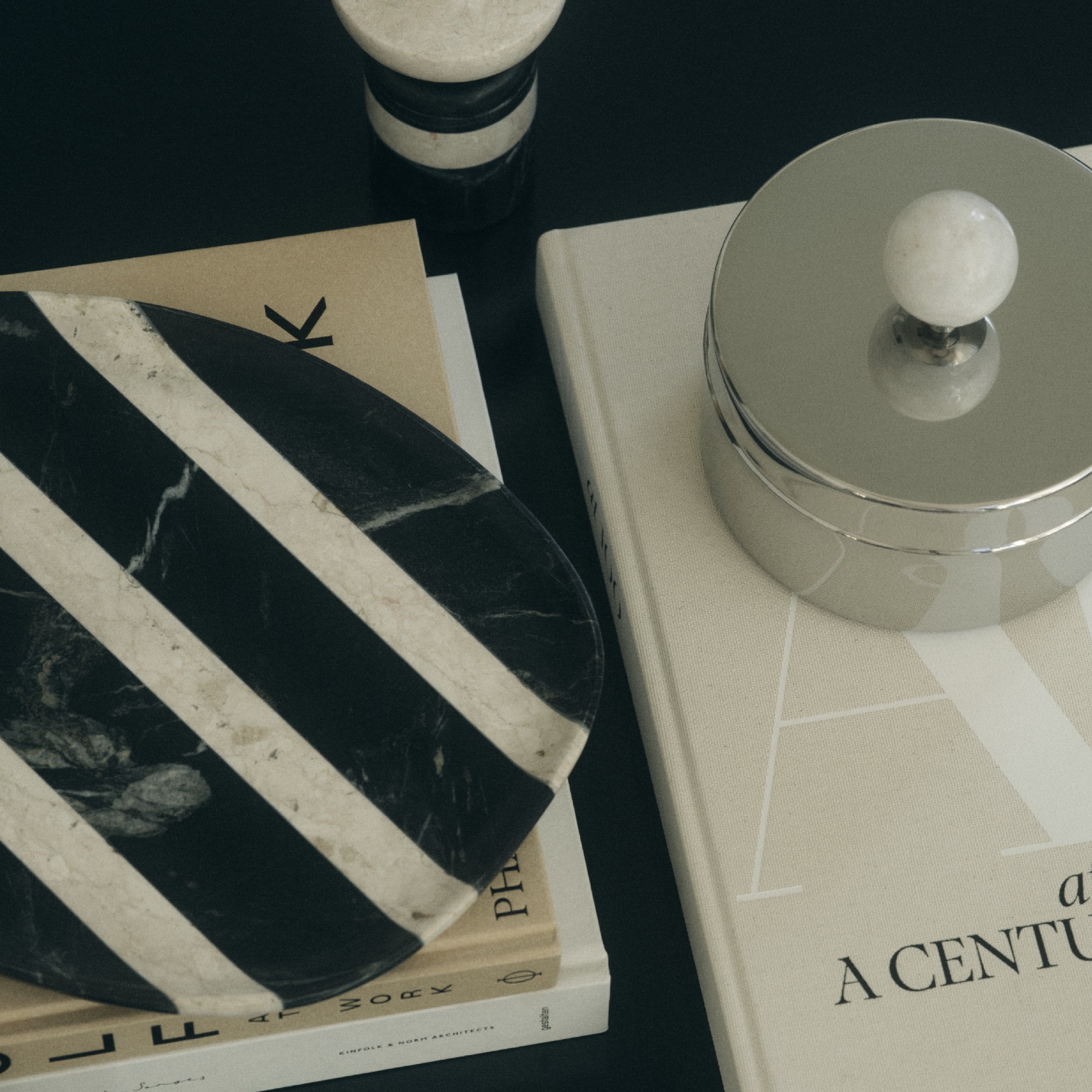 A close-up of a coffee table styled with coffee table books, a striped marble tray and a stainless steel box