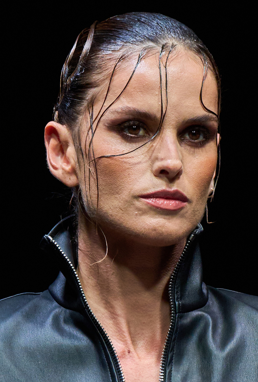 A model at the Laquan Smith SS26 show with wet-look, swept-back hair with tendrils flowing down her face