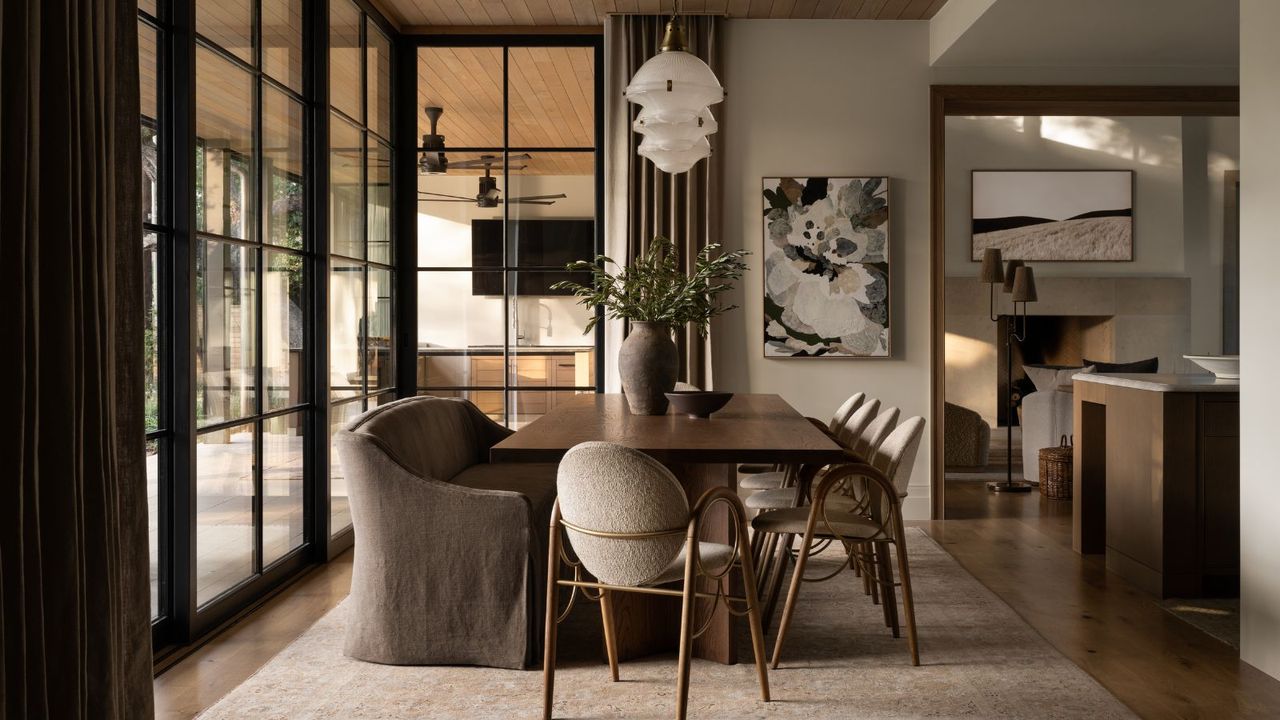 Neutral open dining room with wood table and dining chairs, abstract painting and glass pendants