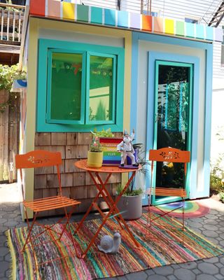 Rainbow-colored she shed with technicolored rug and orange bistro set