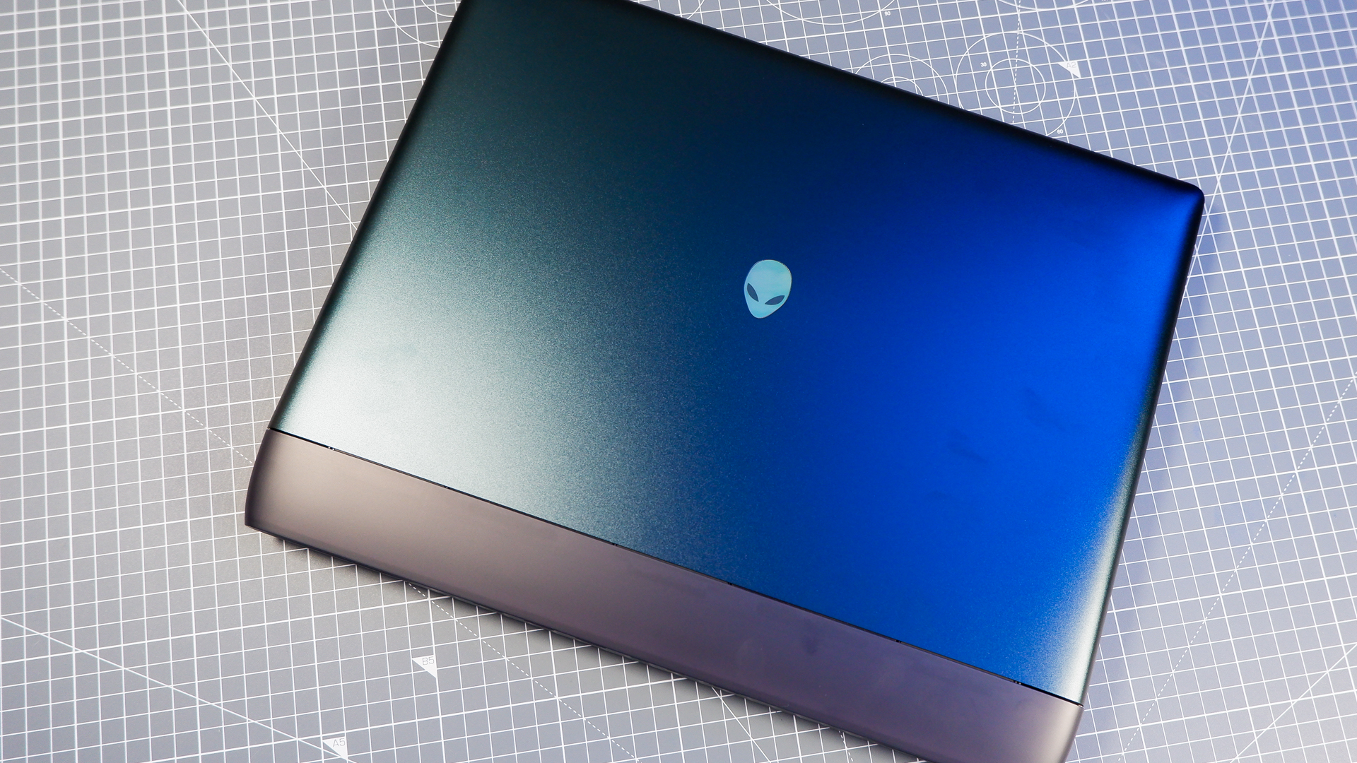 An Alienware 16 Area-51 gaming laptop with RGB lighting in blue on a desk mat.