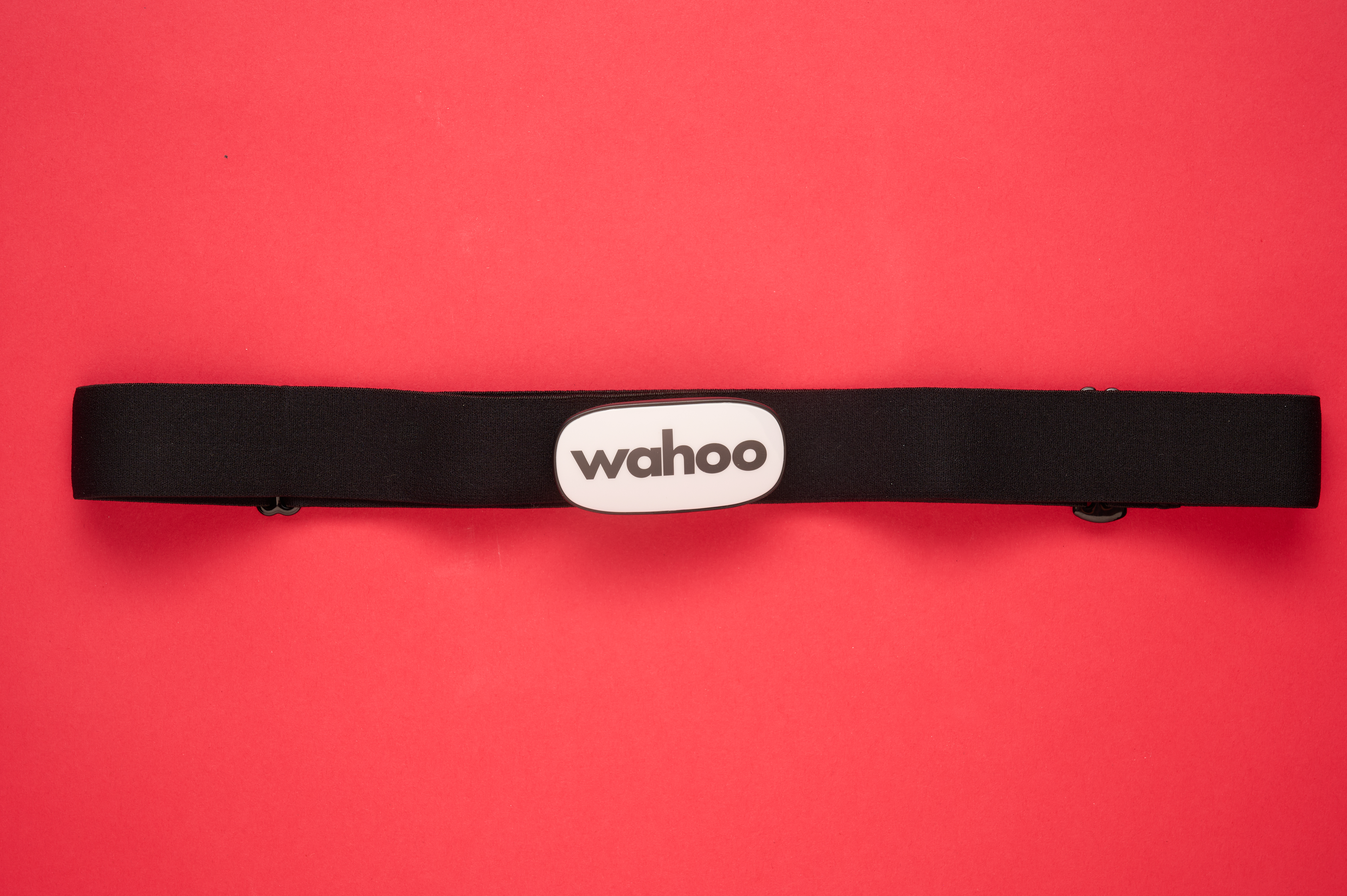 Wahoo Trackr heart rate monitor with its white pill like shaped body and large Wahoo logo across the front in grey, laid flat on a red background