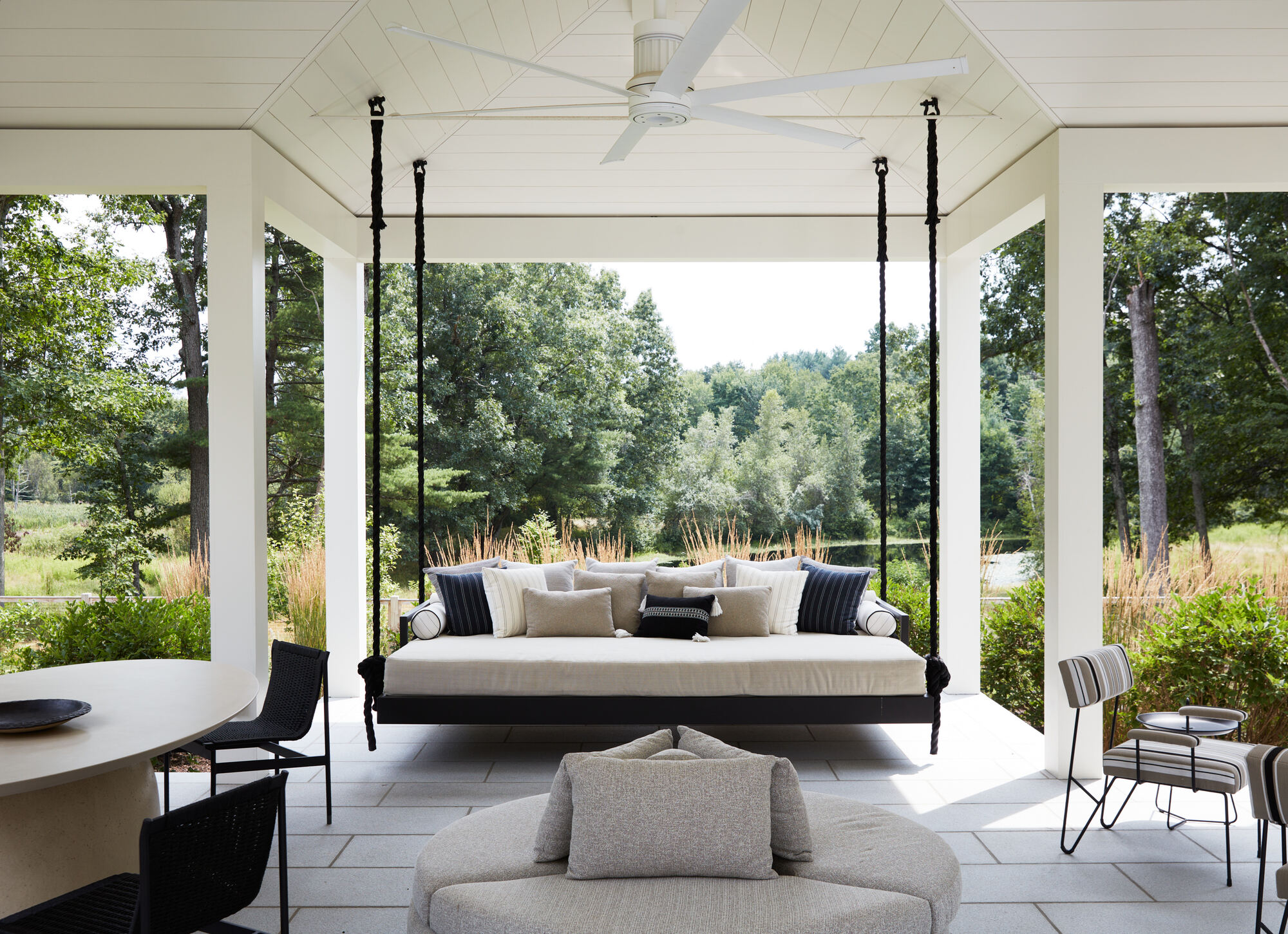 outdoor living room with garden swing chair, dining table, round ottoman-style seat, and armchairs, with views of verdant gardens wrapping the area