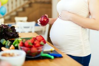 A pregnant woman holding an apple.