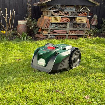 Bosch VISIMOW18V-100 Robot Lawn Mower on grass lawn in front of bug house 