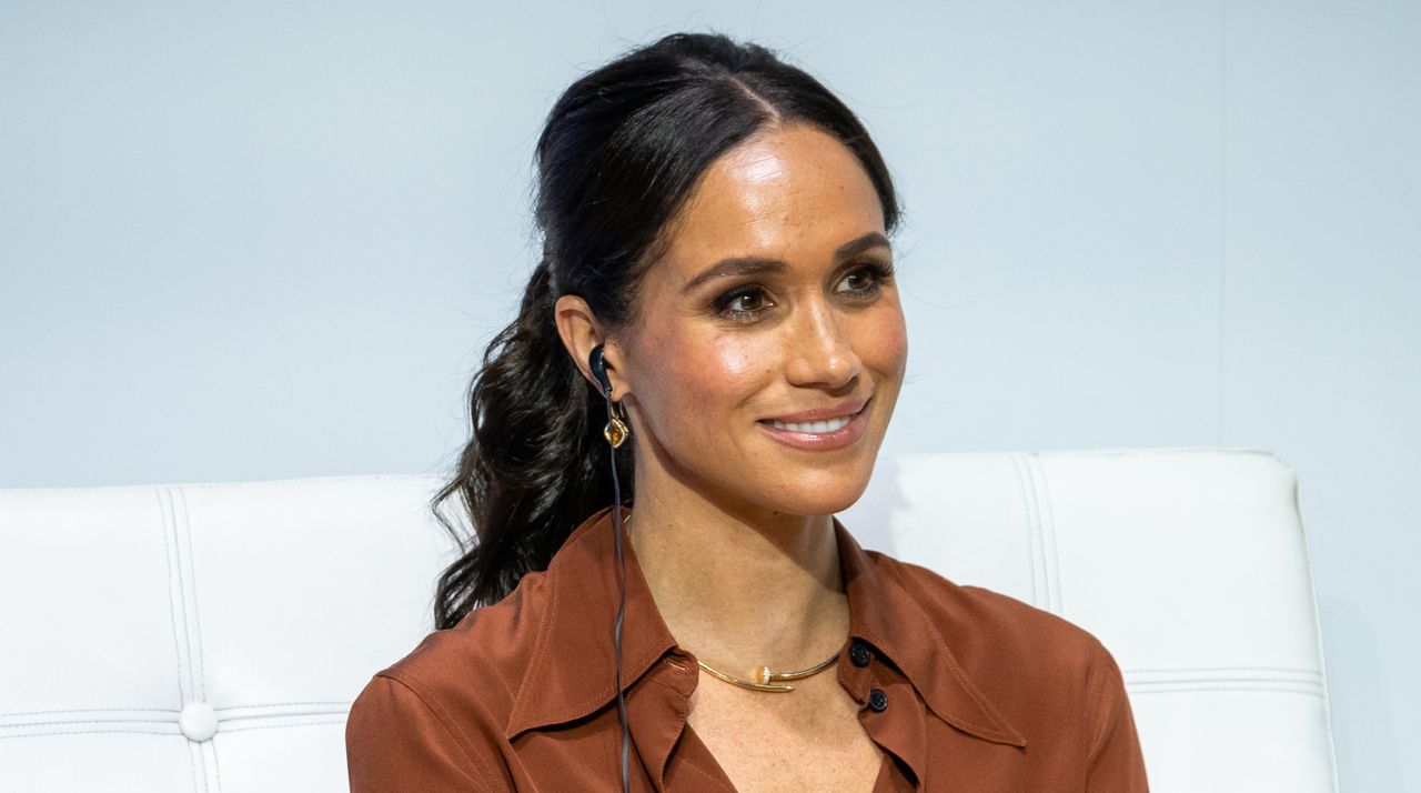 Meghan Markle wears her hair in a ponytail and wears a brown shirt