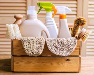 Cleaning set for different surfaces in home including bottles, sprays, cloths and brushes in a wooden crate