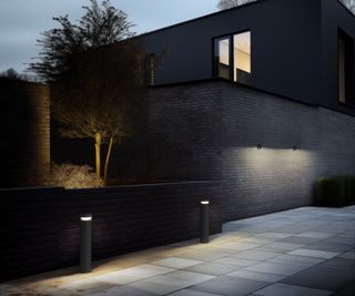 contemporary house with grey brick wall and external lighting by the path, on the walls and up-lighting in the yard where the trees are