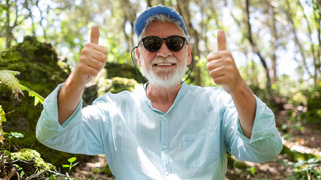 An older man who&#039;s outside smiles and gives two thumbs-up.