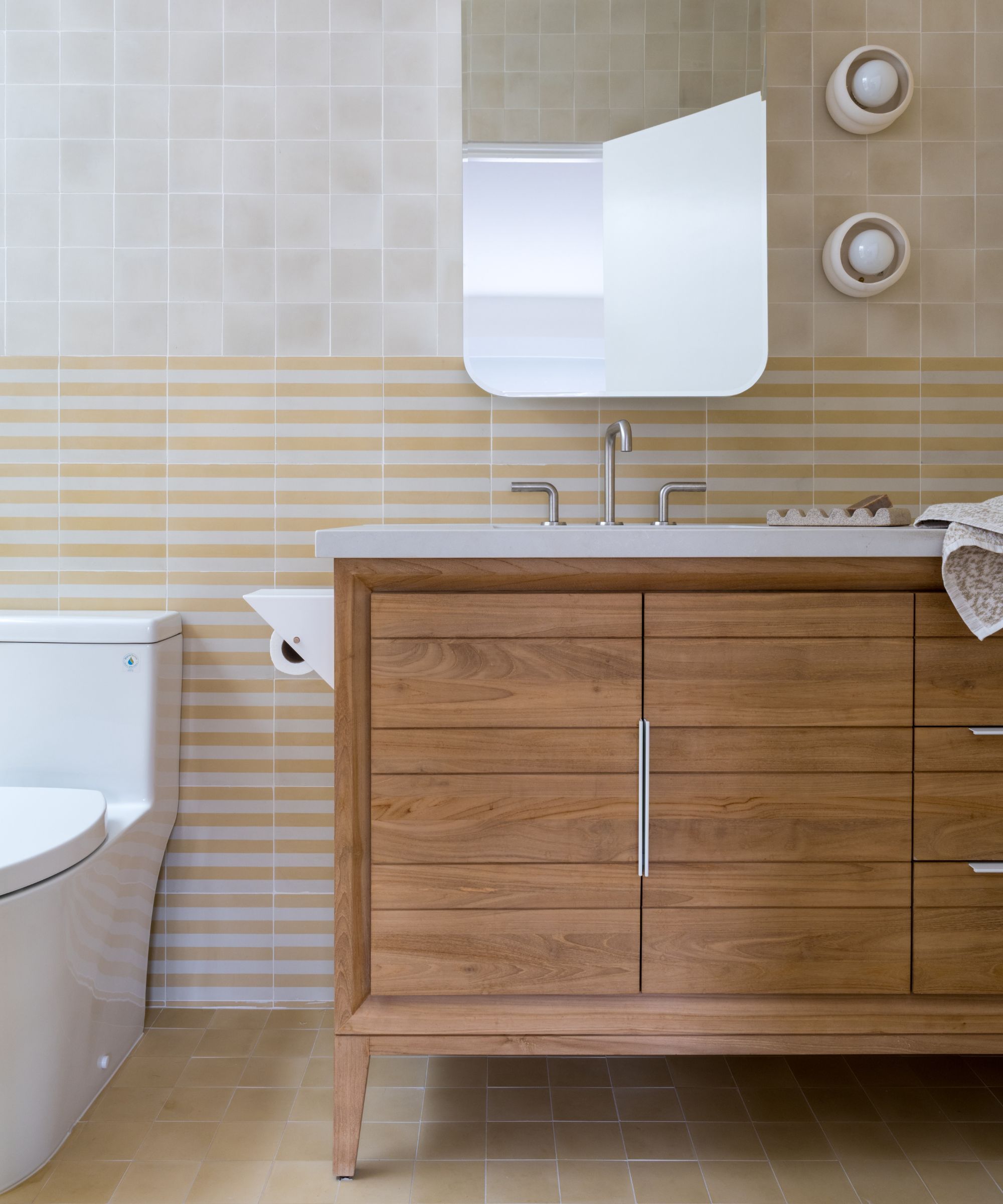 yellow horizontal striped tiles behind toilet and a wooden vanity sink unit