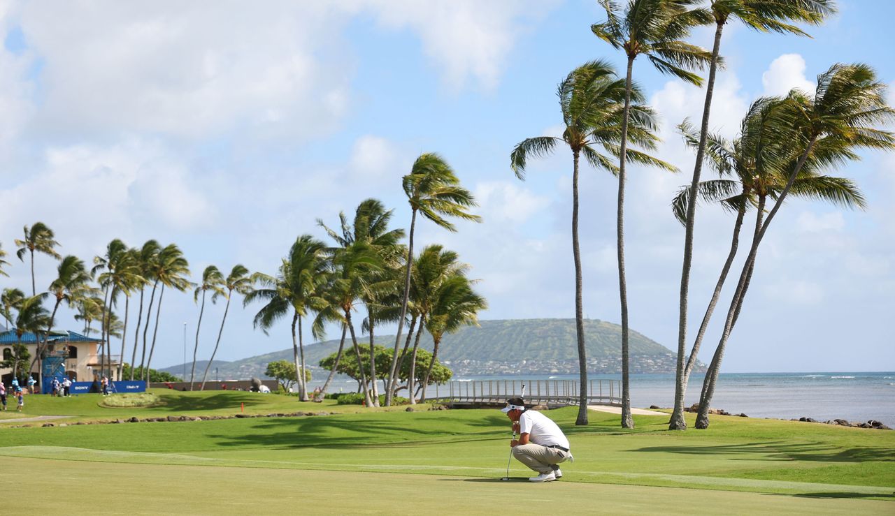 Carl Yuan lines up a putt at the Sony Open, with palm trees fluttering in the background