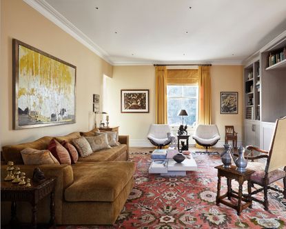 A yellow living room with a dark yellow sofa in front of a light yellow wall and a red patterned rug