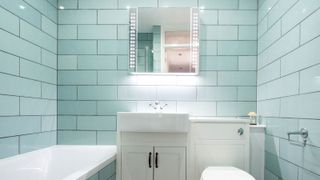 Mint metro tiles in bathroom with bath, vanity unit, toilet and mirror cupboard on wall