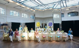 A beautiful decorated long table with golden chairs and colourful cushions with people around the table