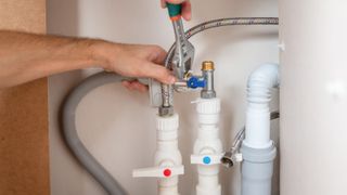 A man uses an adjustable wrench to install a water supply hose in the dishwasher