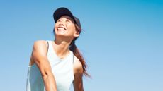 Happy woman wearing sports cap and top playing tennis in the sunshine