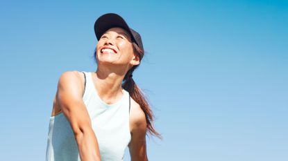 Happy woman wearing sports cap and top playing tennis in the sunshine