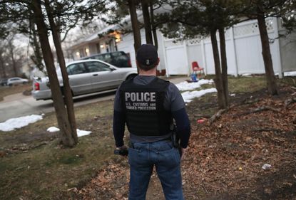 An ICE agent waits outside a house in New York.