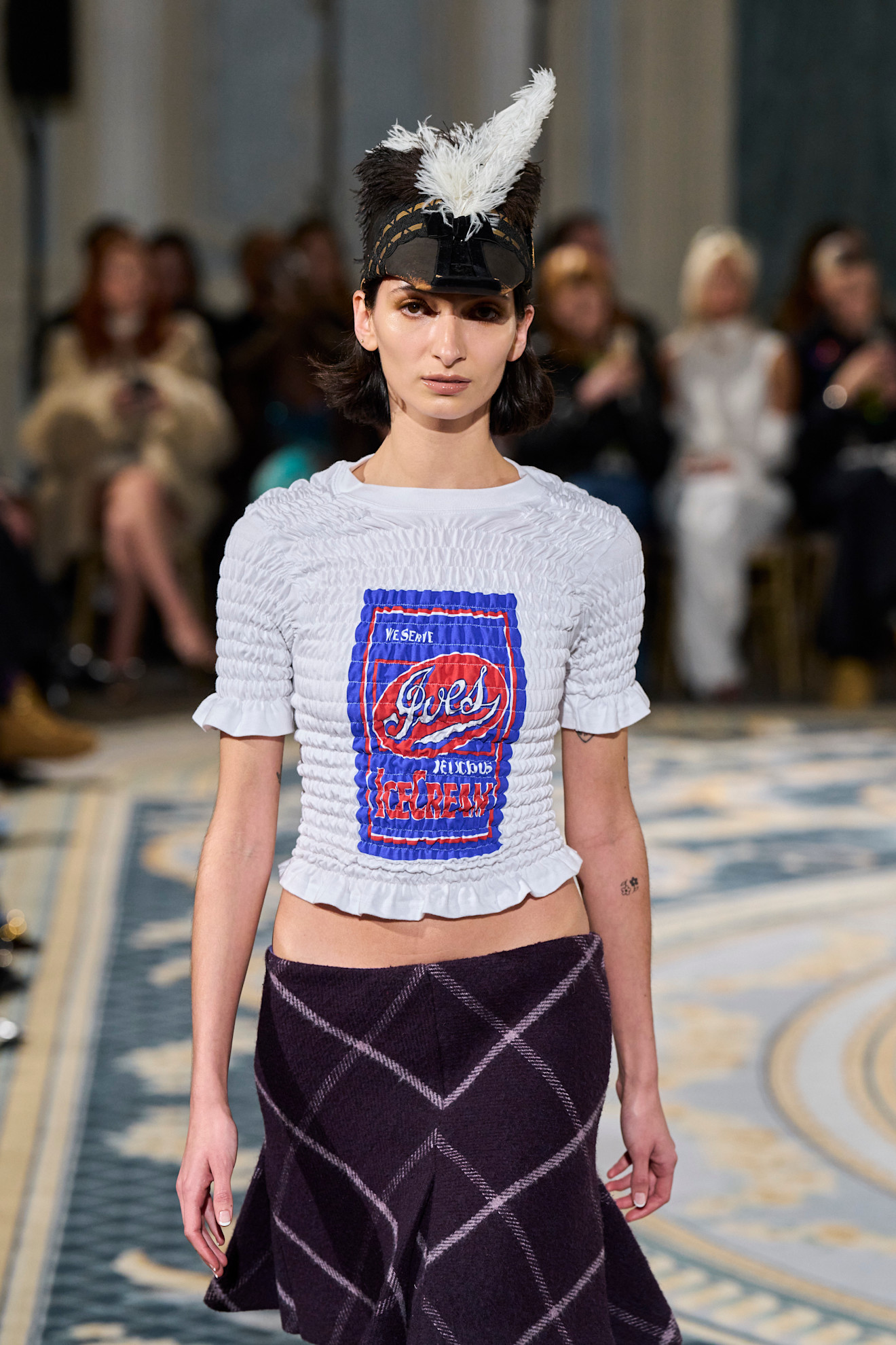 A model wearing a white shirred shirt and plaid skirt