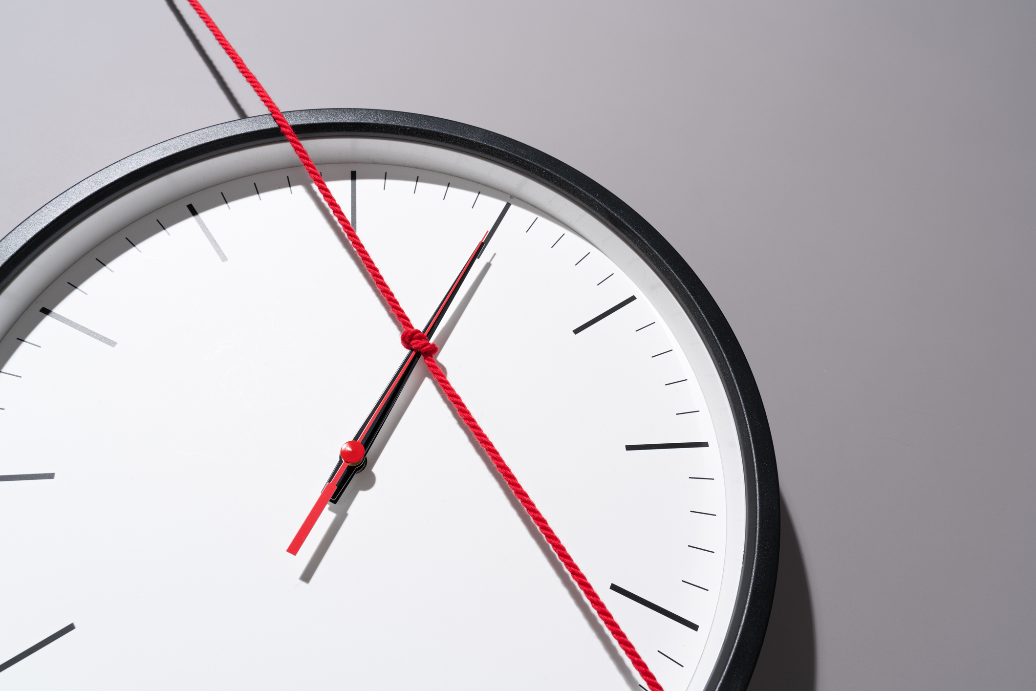 Tied up Clock Hands With a Long Red String on a Gray Background