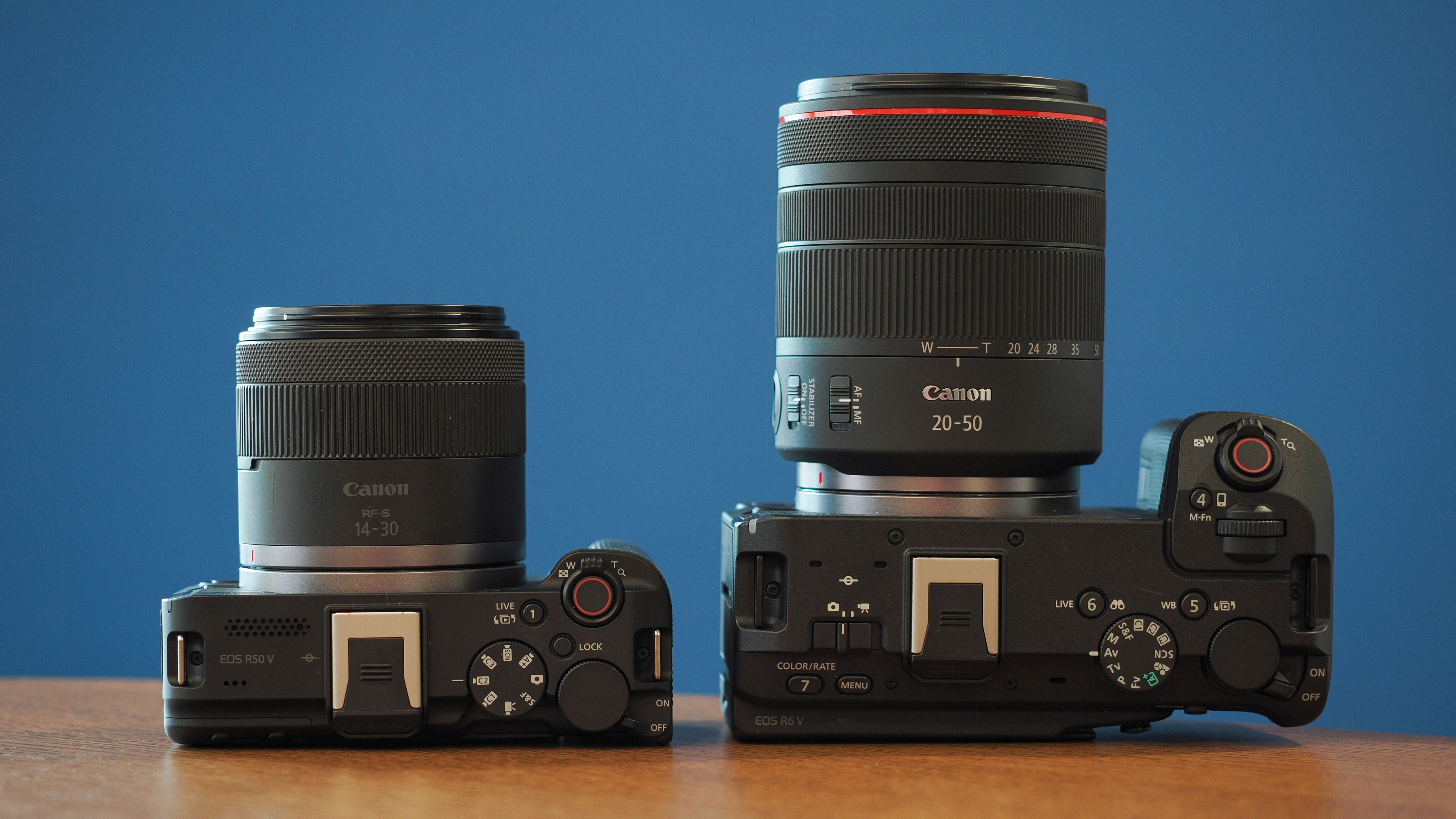 Canon EOS R50 V next to an EOS R6V on a wooden table in front of a blue background