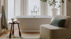 modern bathroom by anthropologie with a large bay window, freestanding bathtub with a large rug, slipper chair, green checkerboard towel and stool