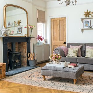 White living room with grey sofa and footstool, open brick fireplace with log burner, over mantle mirror