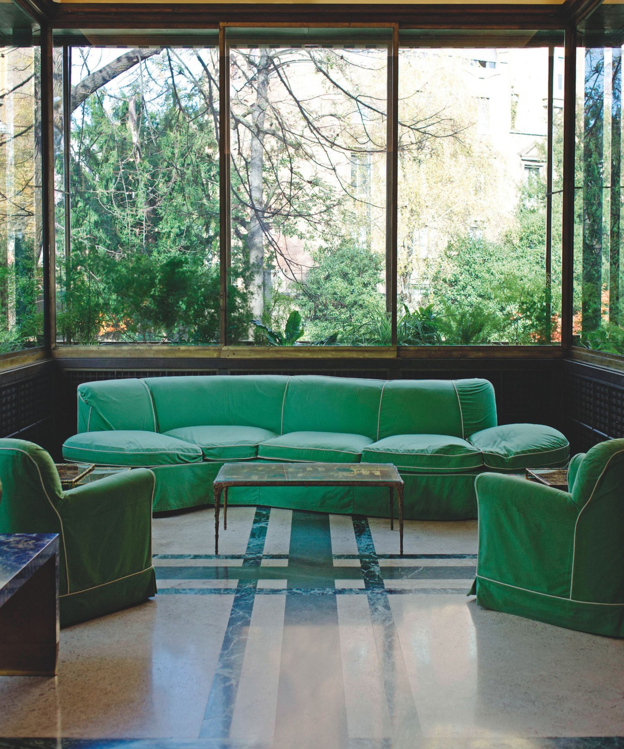 Green living room with sofas, armchairs and greenery beyond