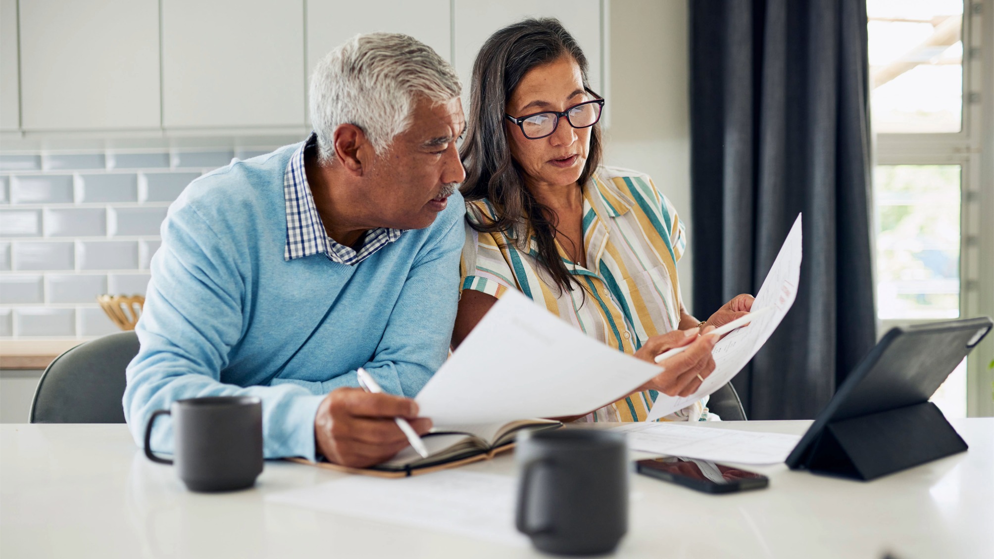 Older couple sitting at their kitchen table reviewing financial documents.