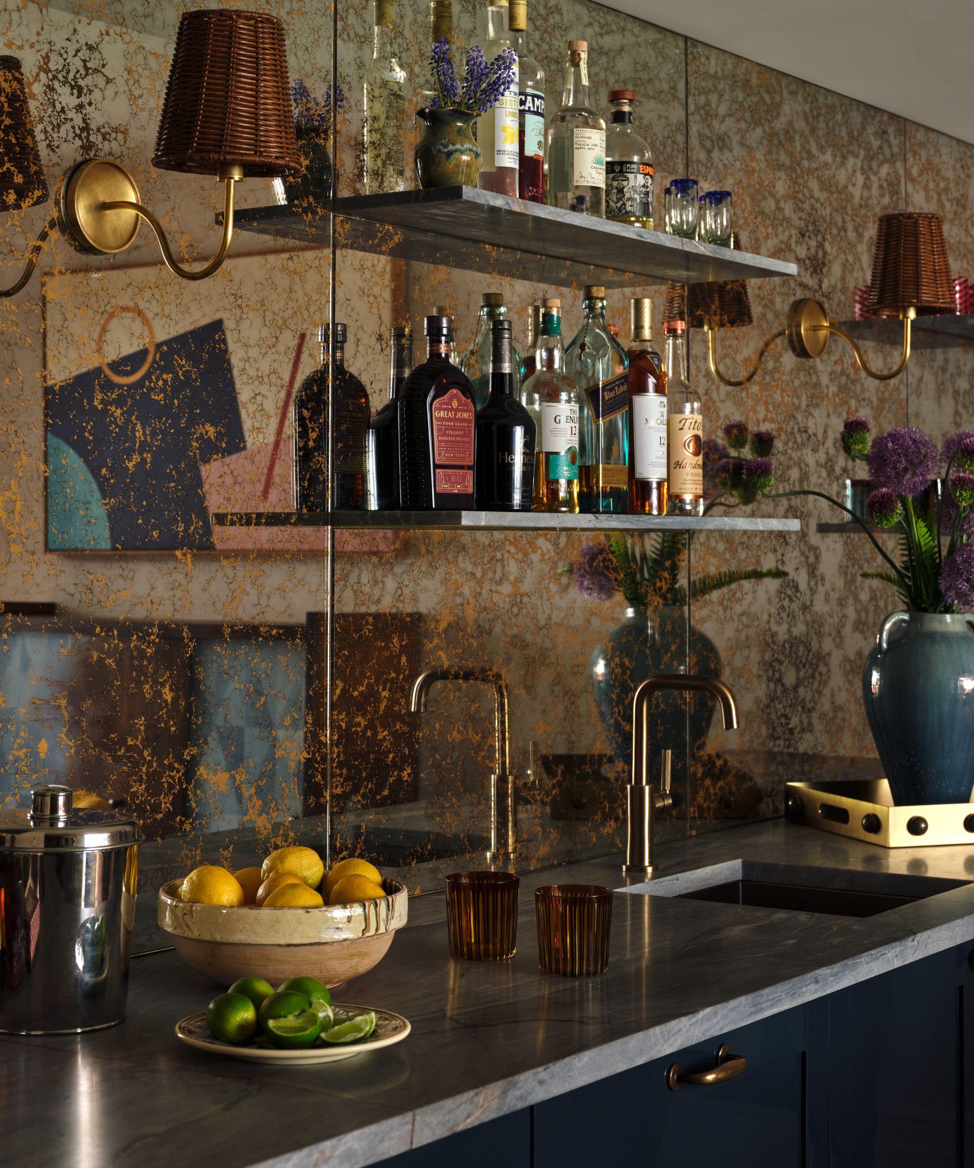 a home bar with a metallic vintage style mirrored backsplash and navy cabinetry and open shelving filled with bottles