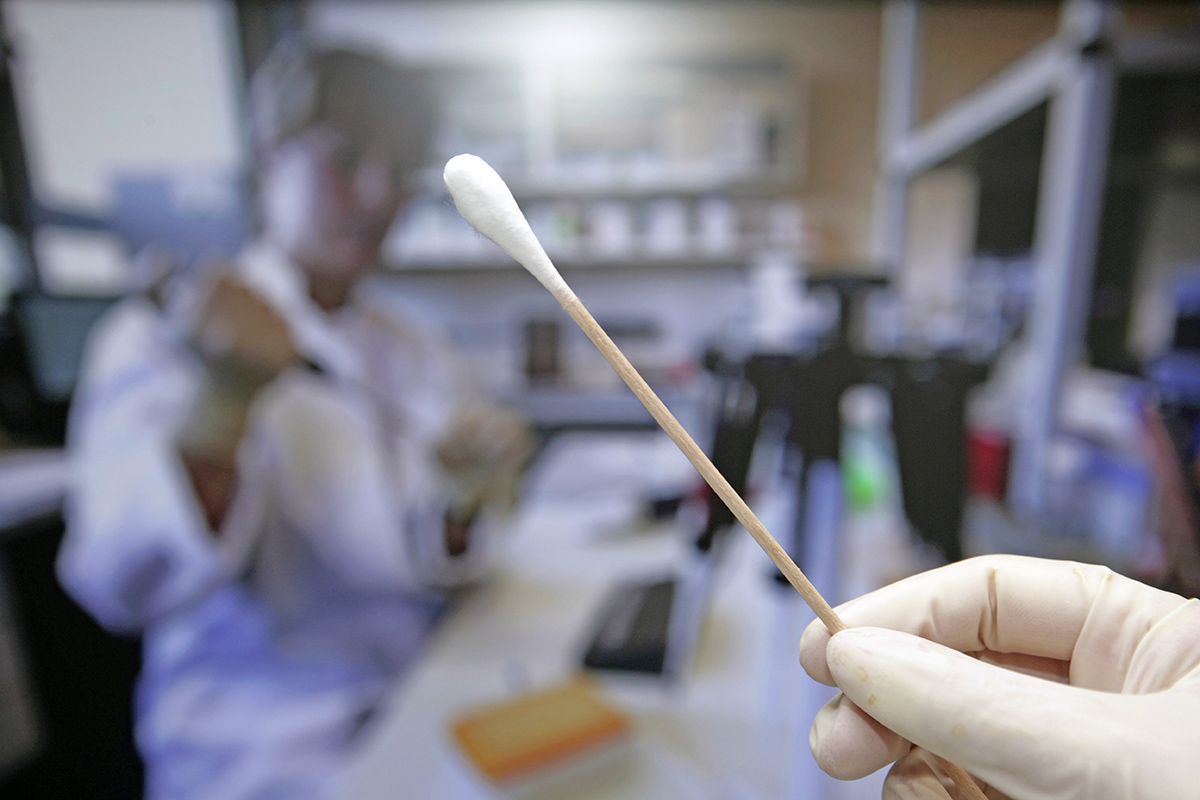 A close-up image of a Q-tip with scientists in a lab.