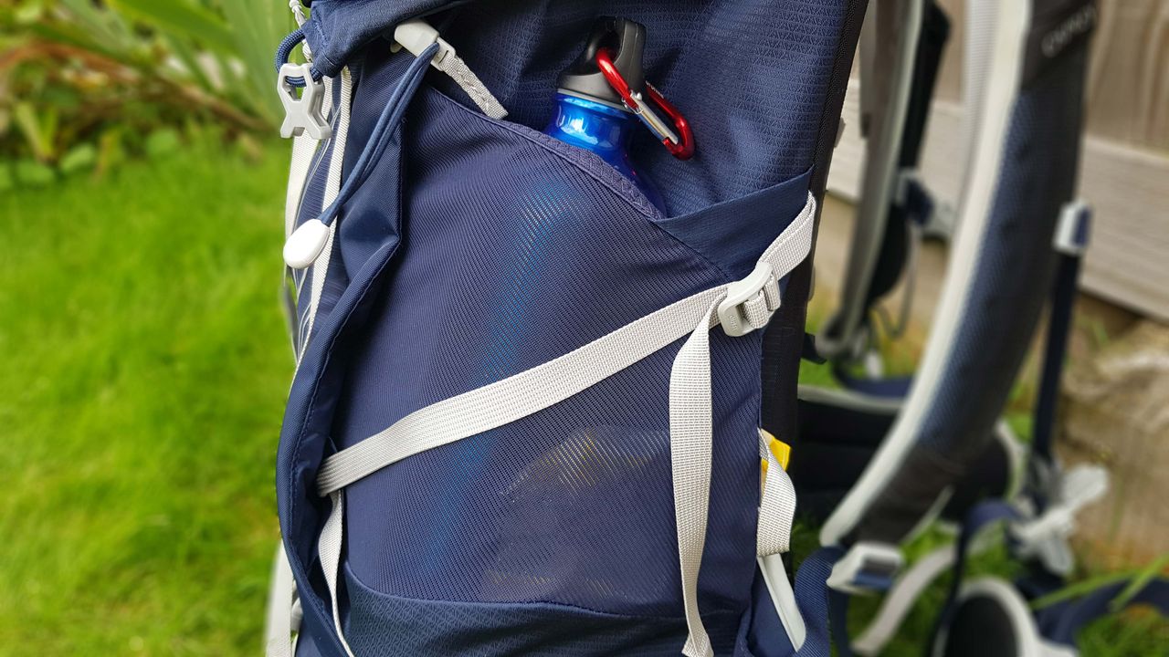 Osprey Talon 55: side pocket with a water bottle sticking through the top access and a sweets packet slightly showing through the side access
