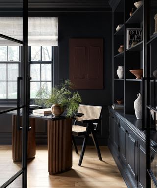 Dark painted room with wooden desk and rattan chair