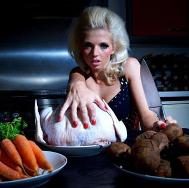 blond woman at table in dark kitchen reaching for raw chicken