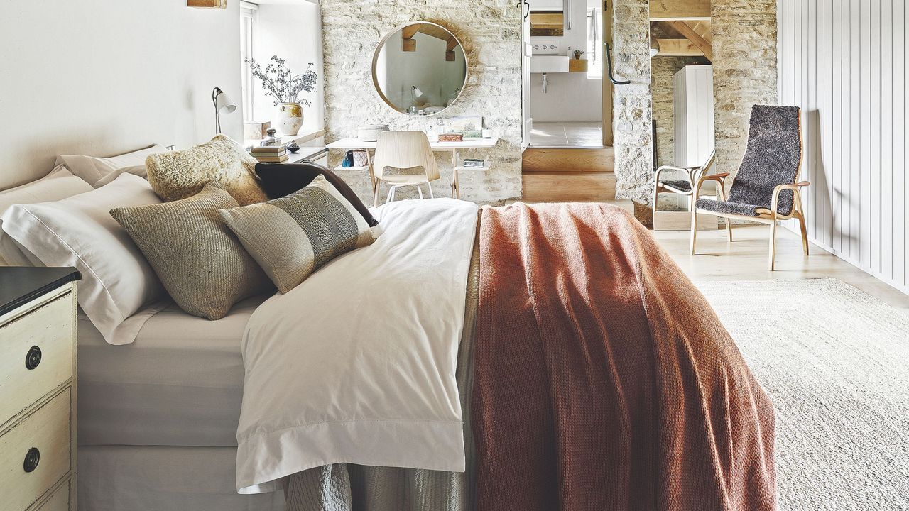 Rustic bedroom with exposed brick walls and a large bed with layered bedding in white, orange and gray