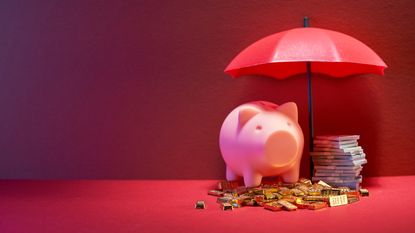 A piggy bank under an umbrella next to a pile of small gold bars and a stack of cash against a red background.