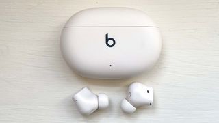 Beats Studio Buds+ in ivory with charging case on a wood background
