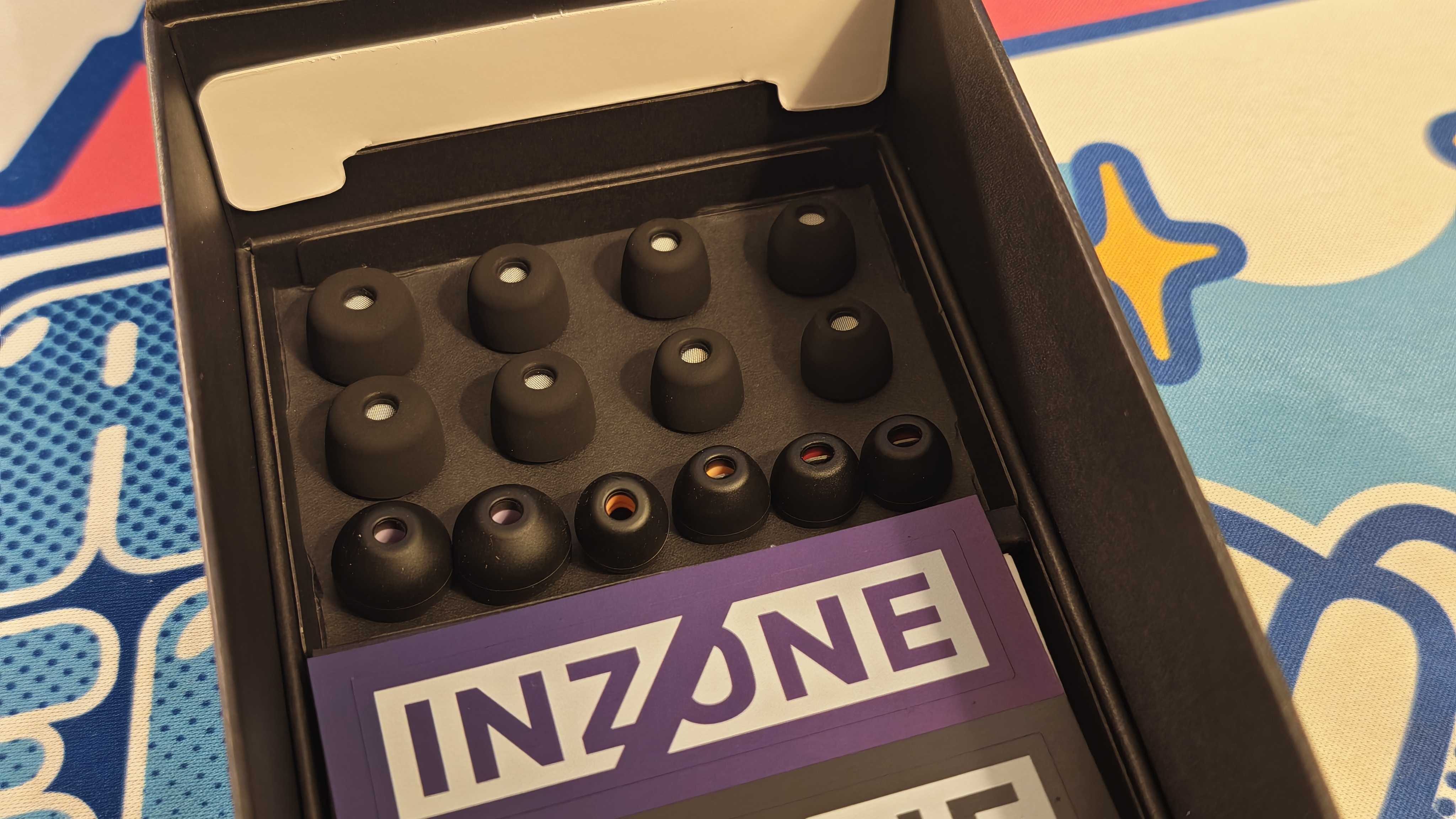 The Sony Inzone E9 gaming earbuds on a colorful desk mat.