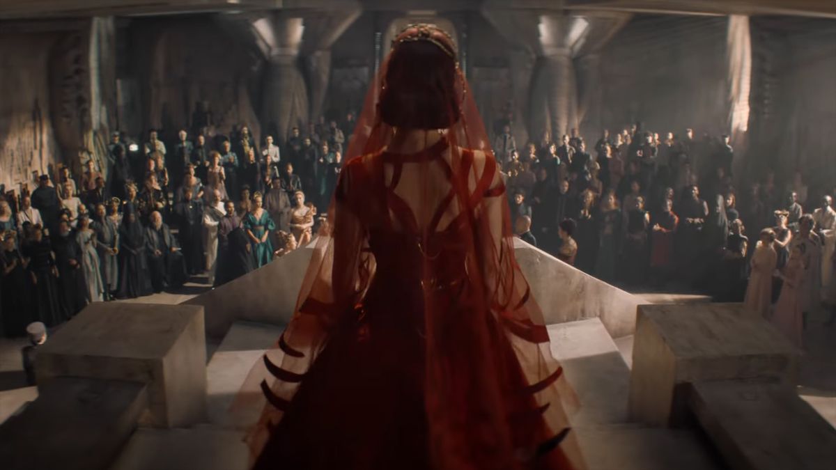 A screenshot of a woman in a red lace dress standing in front of a crowded room in HBO&#039;s Dune: Prophecy TV show