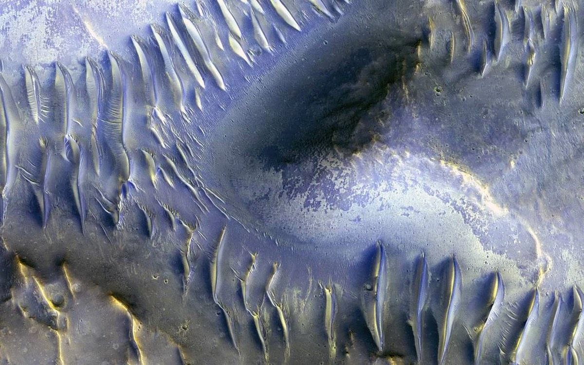 The mound in the center of this image — which was captured by the HiRISE camera aboard NASA&#039;s Mars Reconnaissance Orbiter in April 2009 — appears to have blocked the path of sand dunes as they marched across the scene. 