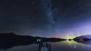 milky way and faint distant aurora borealis shine in a moonless sky above a serene body of water.