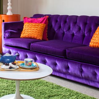 A living room with a purple sofa and orange cushions