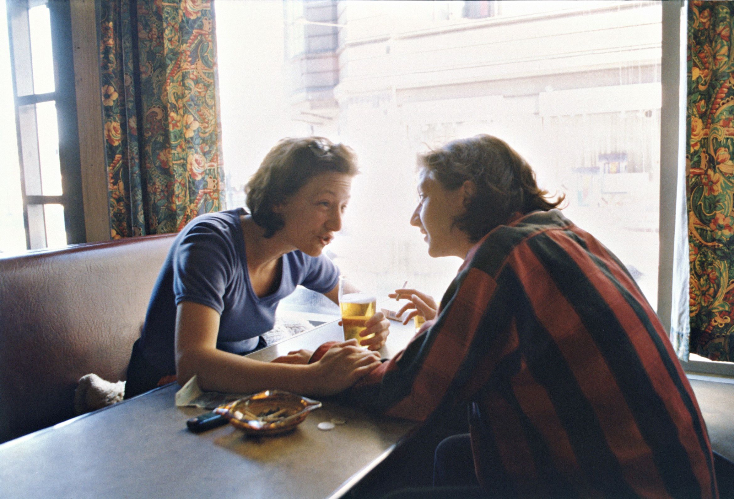 Photograph of two figures talking at table, both of whom are the photographer Vibeke Tandberg