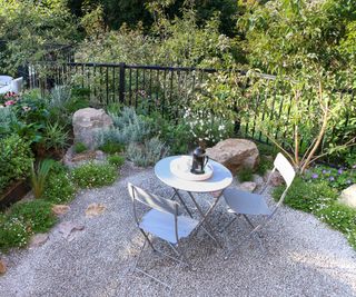 A high angled shot of a small bistro table and chairs on a gravel patio surrounded by planting