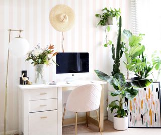pink papered home office with plenty of houseplants, white desk and chair, and a Mac computer