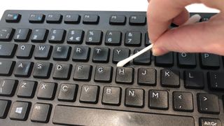 A cotton swab cleaning between the keys on a keyboard