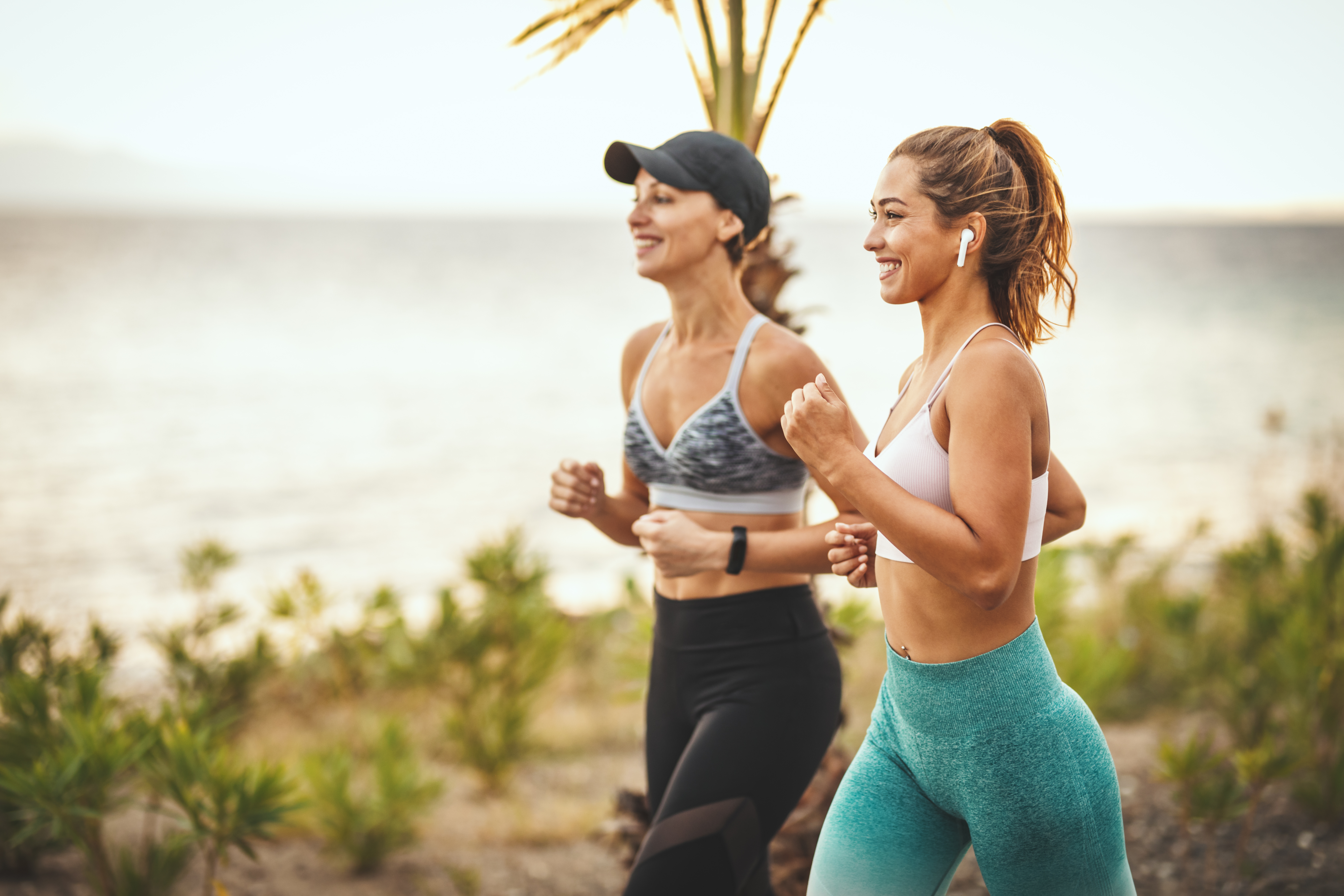 Two women power walking outdoors by the ocean smiling